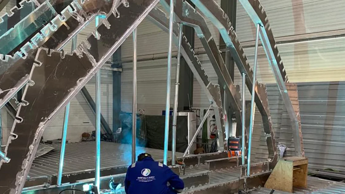 A RAM welder working on an aluminium hull section frame in a shipbuilding workshop.