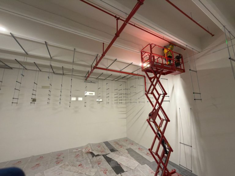 RAM project: Installer fixing overhead supports from a raised red scissor lift