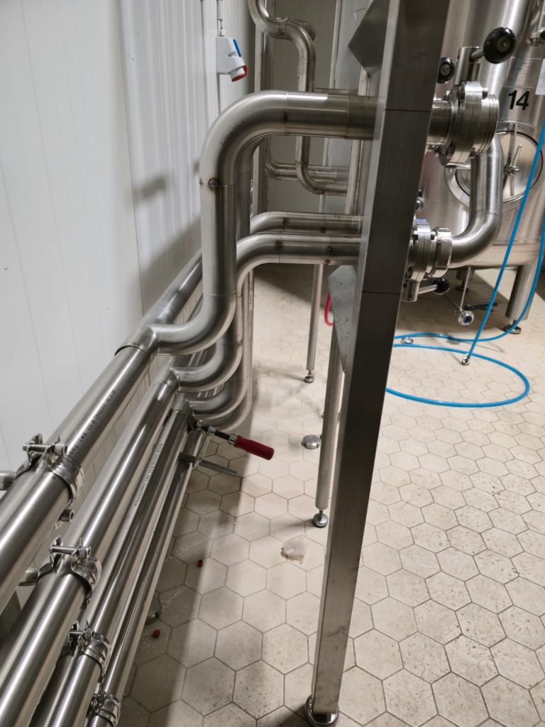 RAM project: Parallel stainless steel pipes and bends routed beside brewery tanks