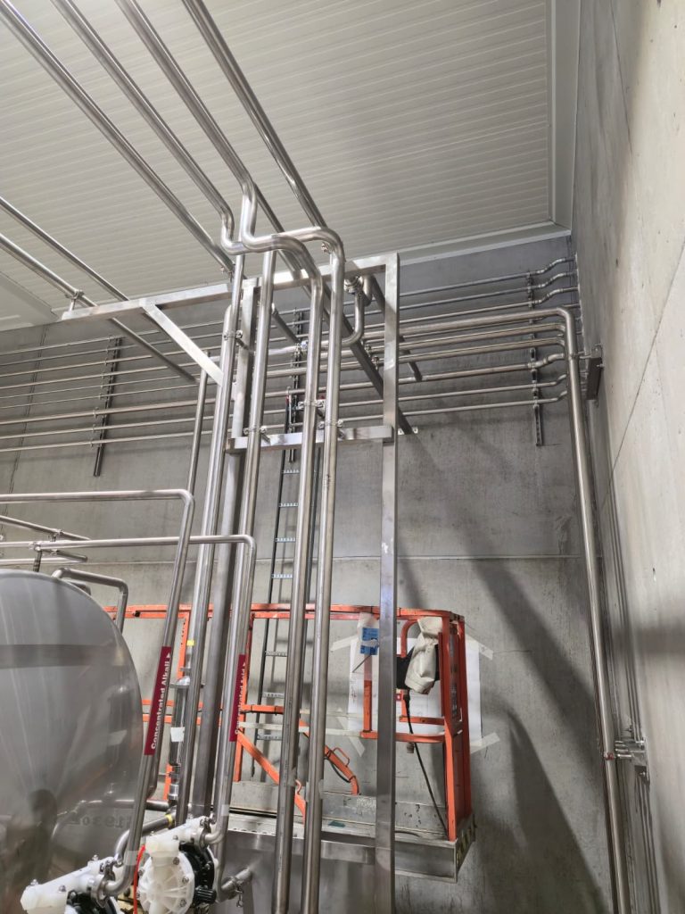 RAM project: Vertical and overhead stainless steel pipes with supports beside brewery process tanks