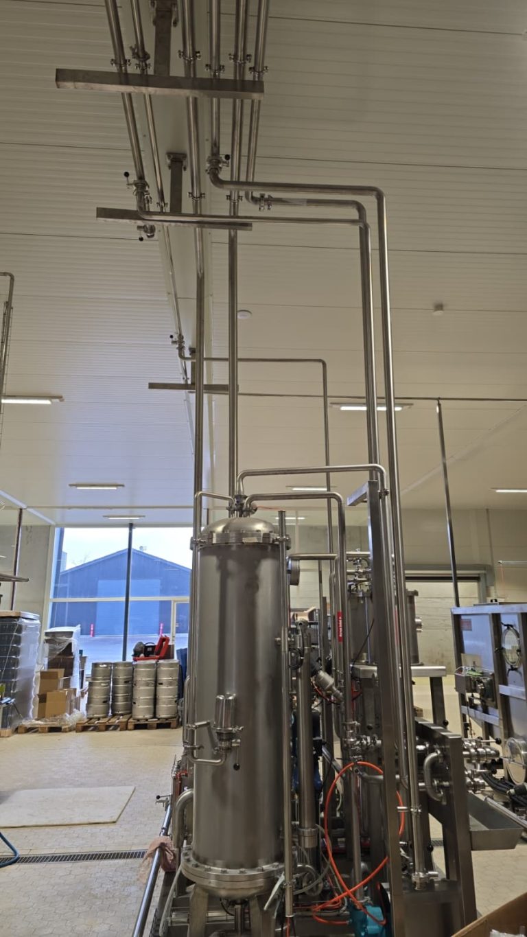RAM project: Vertical brewery process vessel with overhead stainless steel piping and keg storage behind