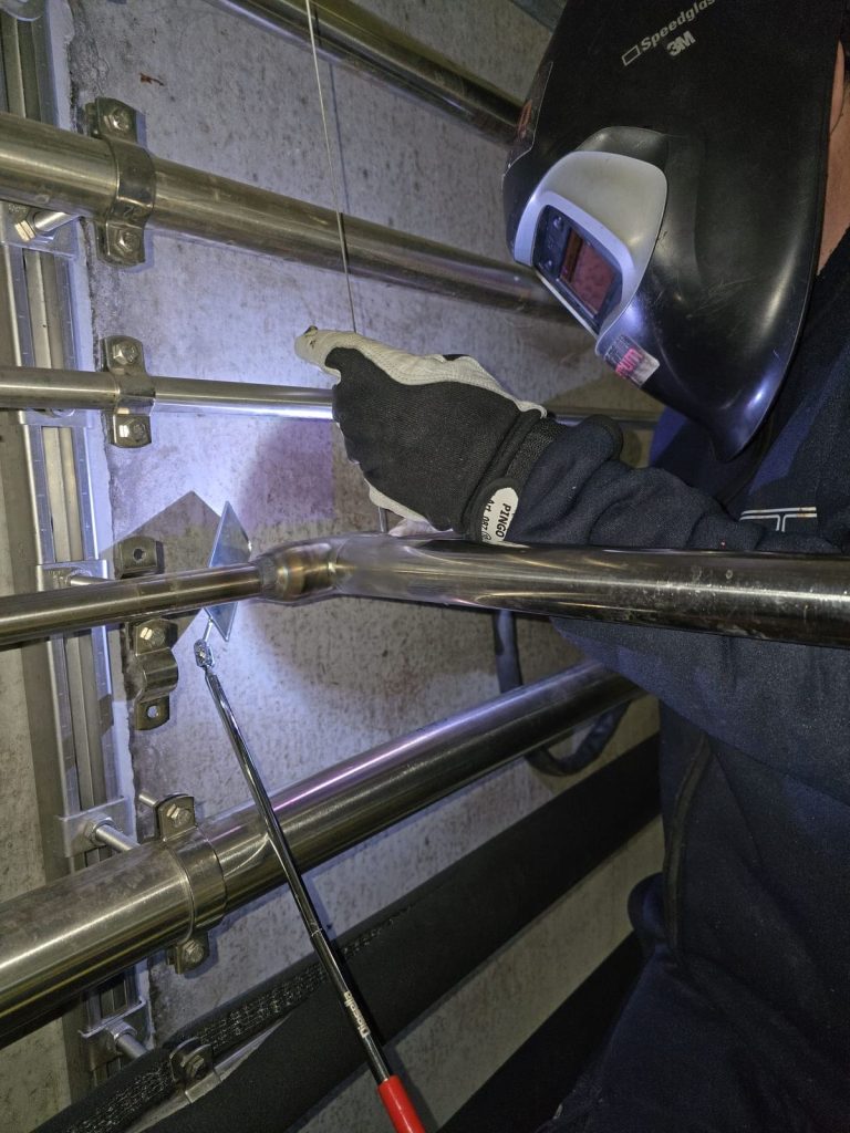 RAM project: Welder working on wall mounted stainless steel pipework at a brewery in Denmark